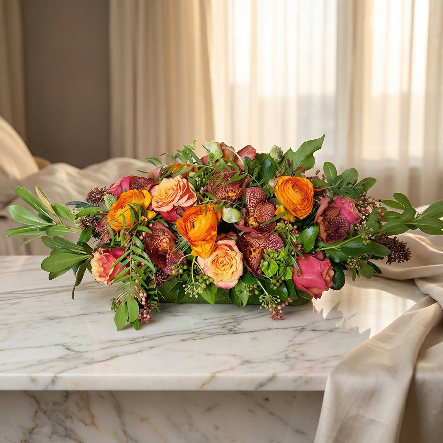 A low, lush arrangement of orange ranunculus, peach roses, and burgundy orchids in a green container - TJ Flowers NYC