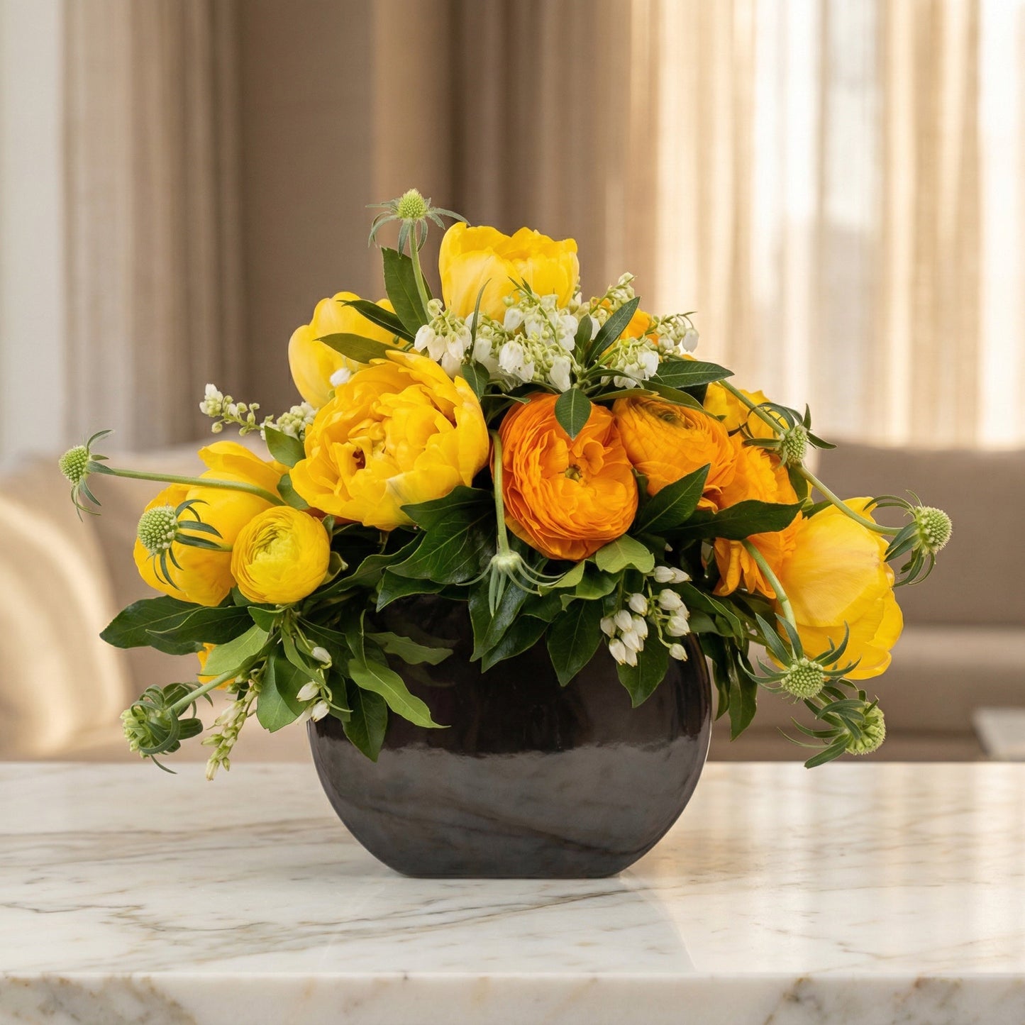 Yellow tulips and orange ranunculus in a dark round vase on a marble table - TJ Flowers NYC