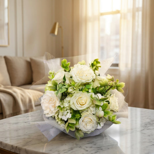 Elegant white roses and green accent flowers in a wrapped bouquet on a marble table in a bright room - TJ Flowers NYC