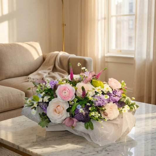 Elegant arrangement with soft pink ranunculus, roses, lavender purple orchids, and white filler flowers in a low container - TJ Flowers NYC