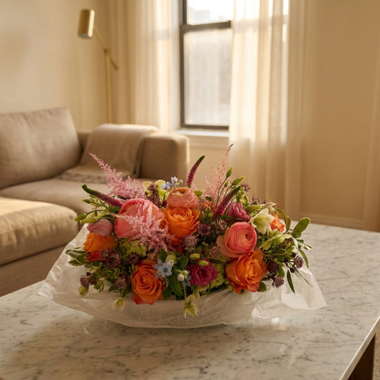 Vibrant arrangement of orange roses, pink ranunculus, and green hydrangeas in a low white ceramic vase - TJ Flowers NYC