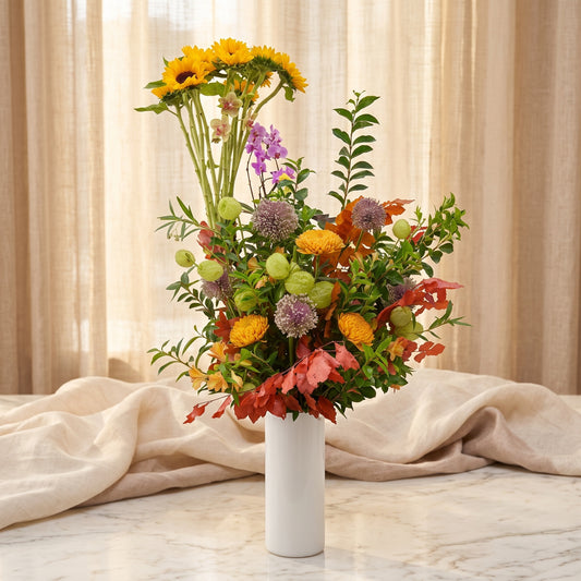 Tall autumn arrangement with sunflowers, allium, pincushion protea and fiery fall foliage in a white cylinder vase - TJ Flowers NYC