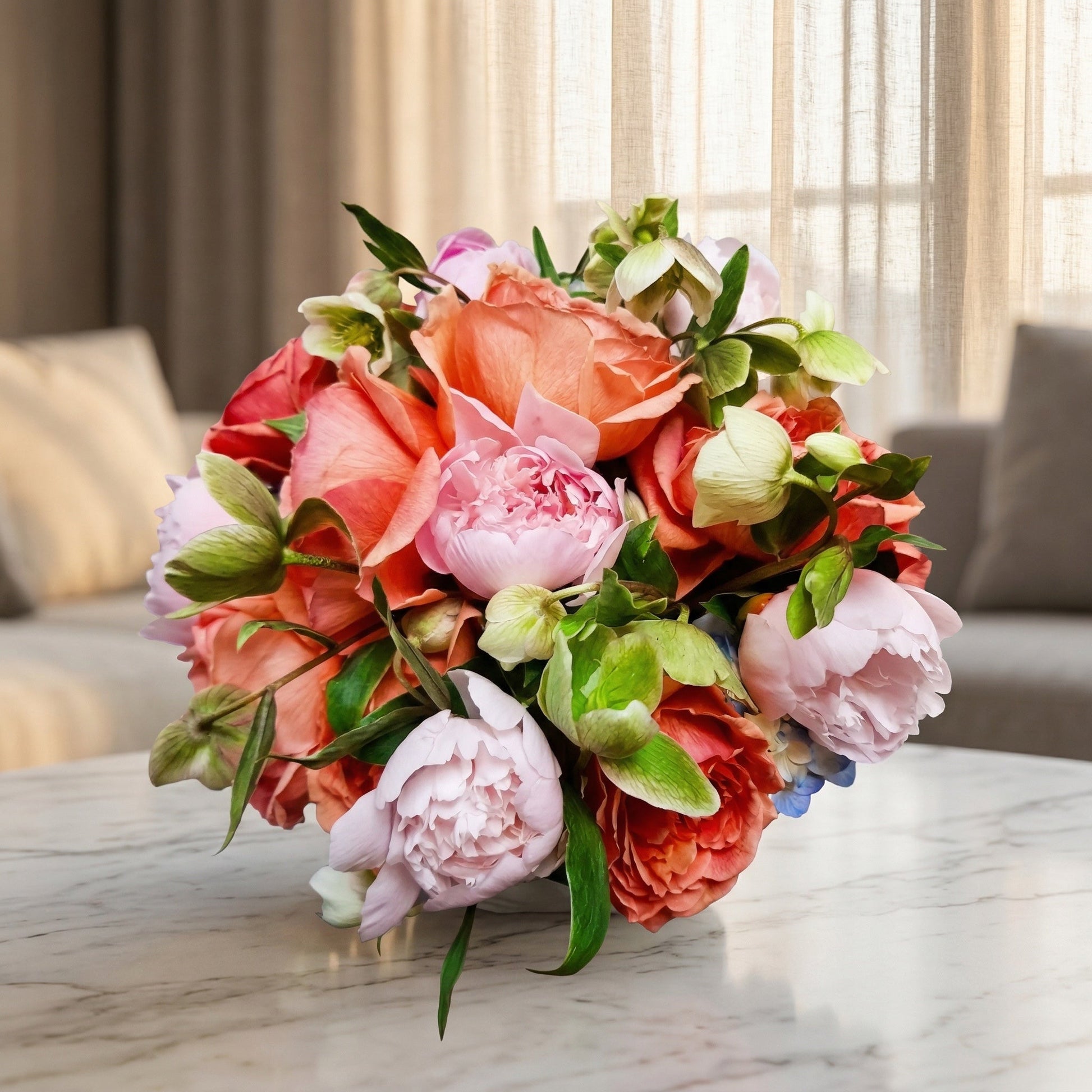 A lush bouquet of coral roses, pink peonies, and green hellebores on a marble table. - TJ Flowers NYC