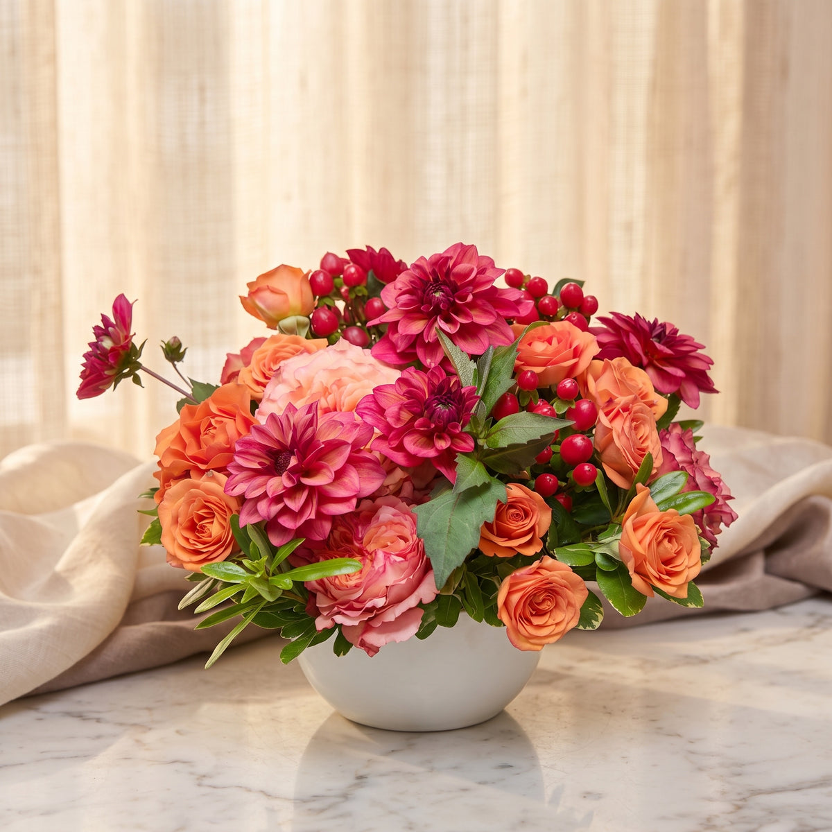 Coral and raspberry dahlias with orange spray roses and red hypericum berries in a white bowl - TJ Flowers NYC
