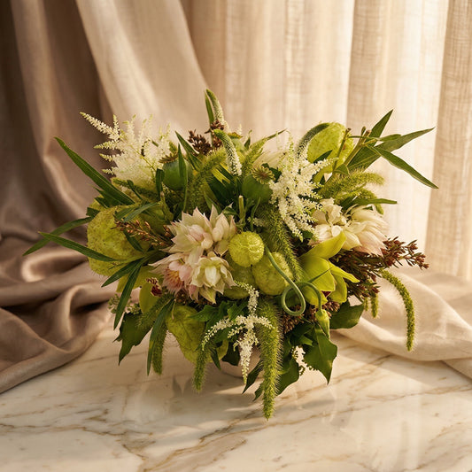 A lush green and white bouquet with orchids, astilbe, and unique textures on a marble table. - TJ Flowers NYC