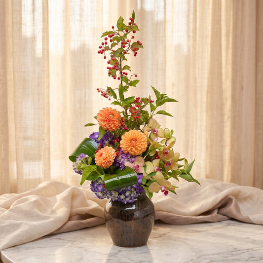 Orange dahlias with peach cymbidium orchids, purple hydrangea and red berry branches in a bronze ceramic vase - TJ Flowers NYC