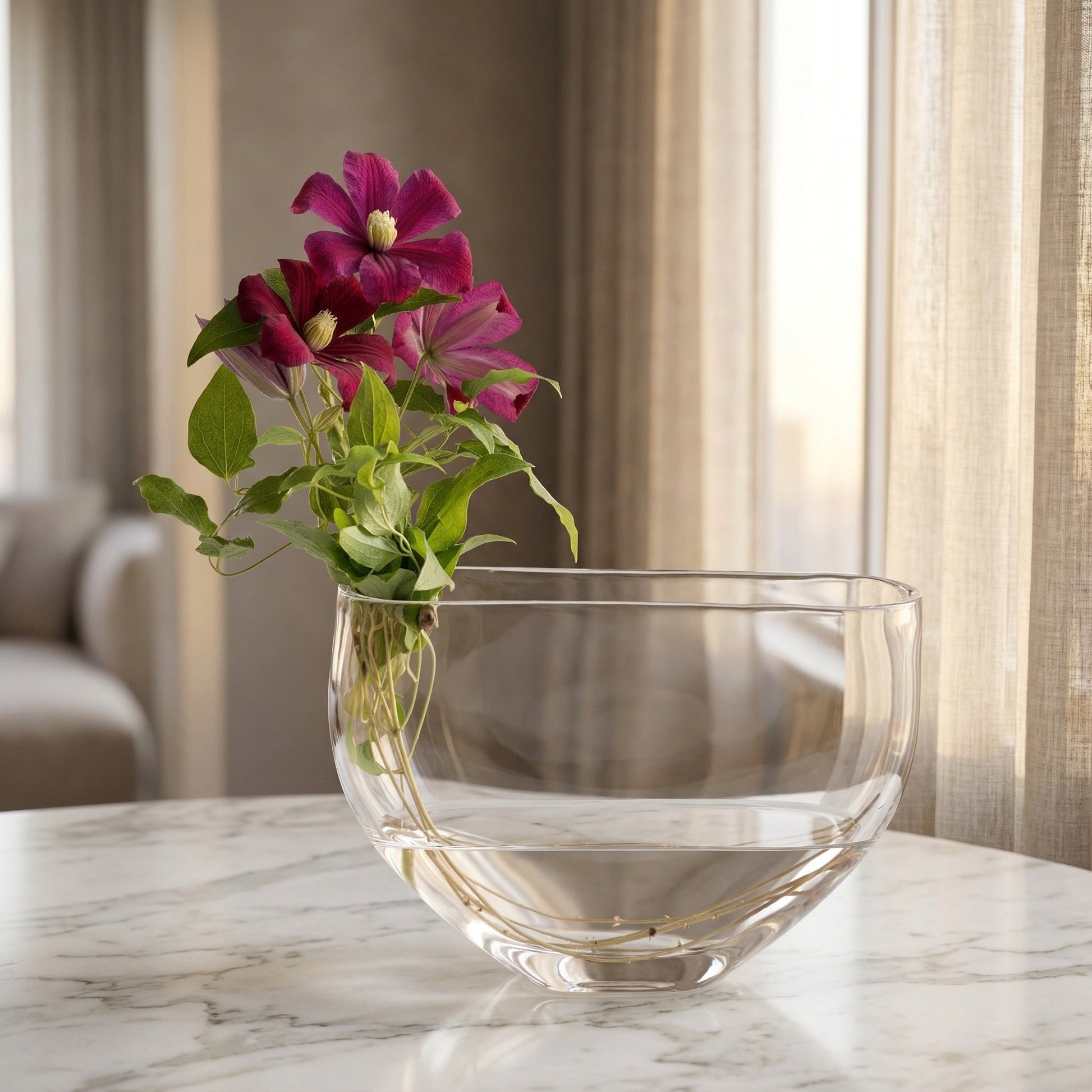 Deep purple clematis flowers in a modern clear glass bowl vase on a marble table. - TJ Flowers NYC
