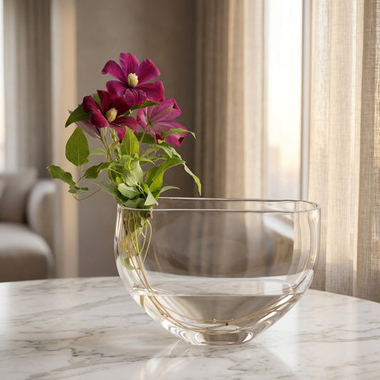 Deep purple clematis flowers in a modern clear glass bowl vase on a marble table. - TJ Flowers NYC