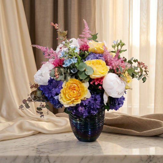 Mixed bouquet with yellow roses, white peonies, and purple hydrangeas in a dark ribbed vase - TJ Flowers NYC