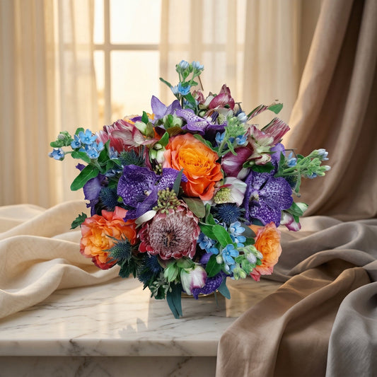 Vibrant bouquet with purple orchids, orange roses, and blue accents on a marble table - TJ Flowers NYC