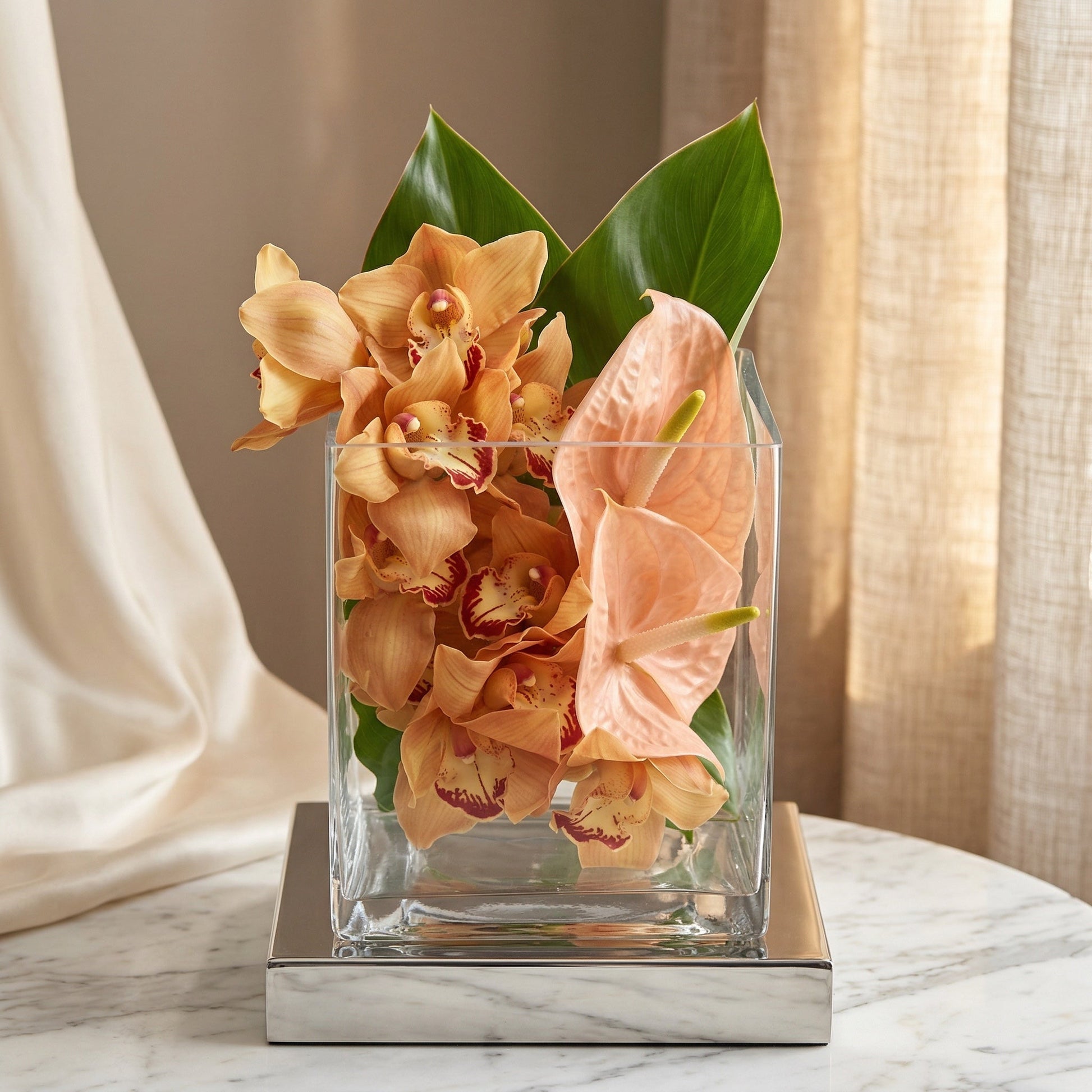 Peach cymbidium orchids and anthurium in a modern square glass vase on a marble table - TJ Flowers NYC