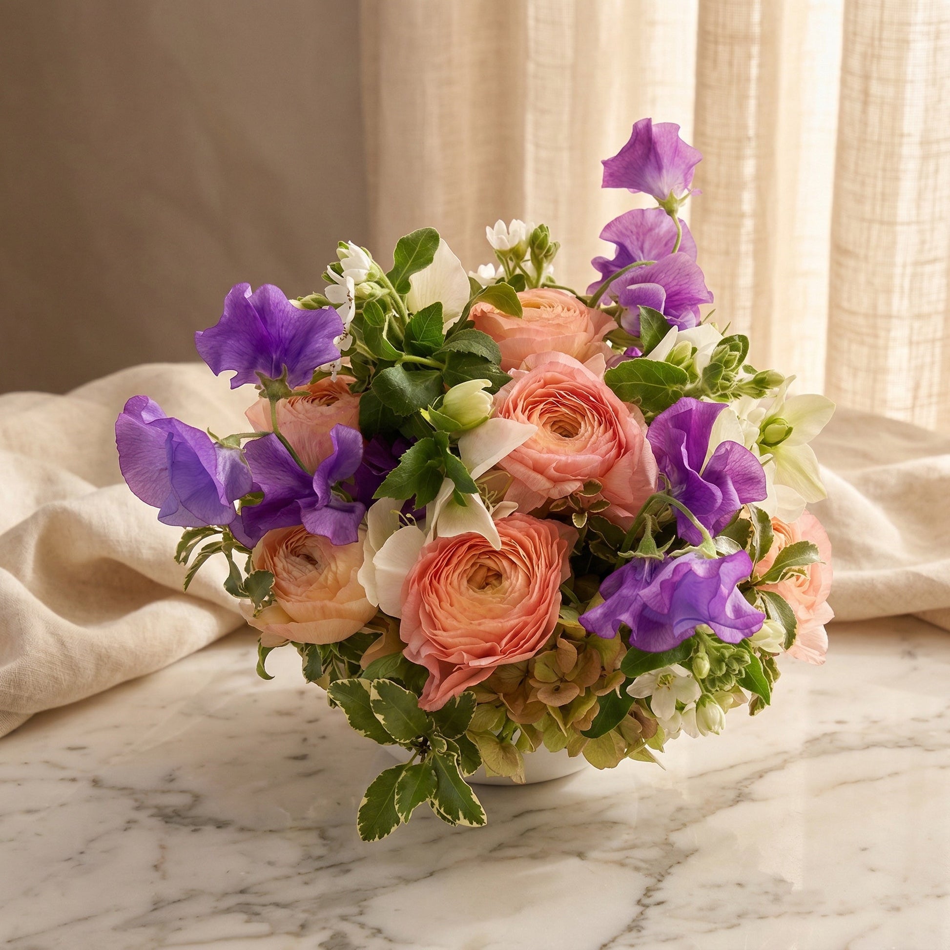 Pastel ranunculus, purple sweet peas, and green hydrangeas in a white vase - TJ Flowers NYC