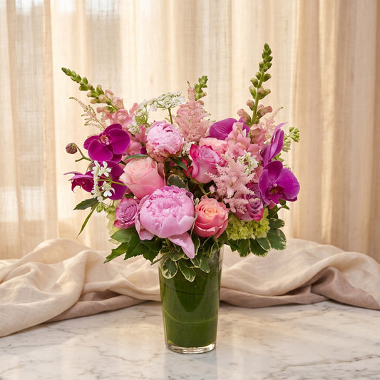 Tall arrangement of pink peonies with magenta phalaenopsis orchids, pink snapdragons and astilbe in a leaf-lined cylinder vase - TJ Flowers NYC