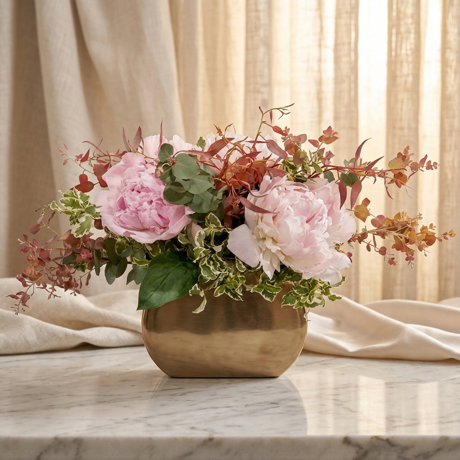 Lush pink peonies and mixed eucalyptus in a modern gold vase on a marble table. - TJ Flowers NYC
