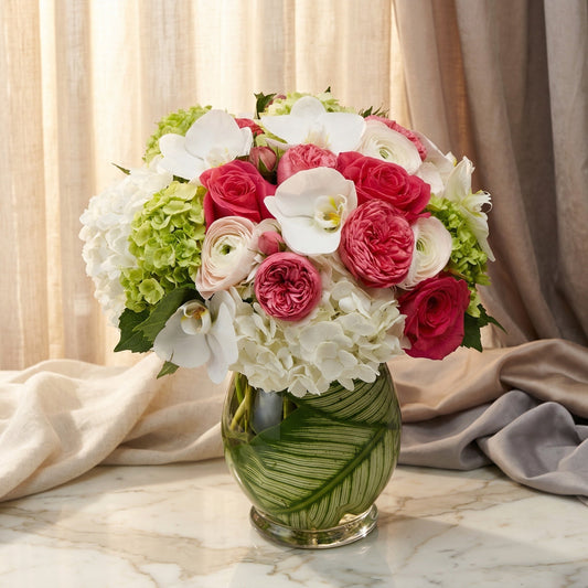 Pink roses, white orchids, and green hydrangeas in a leaf-lined glass vase - TJ Flowers NYC