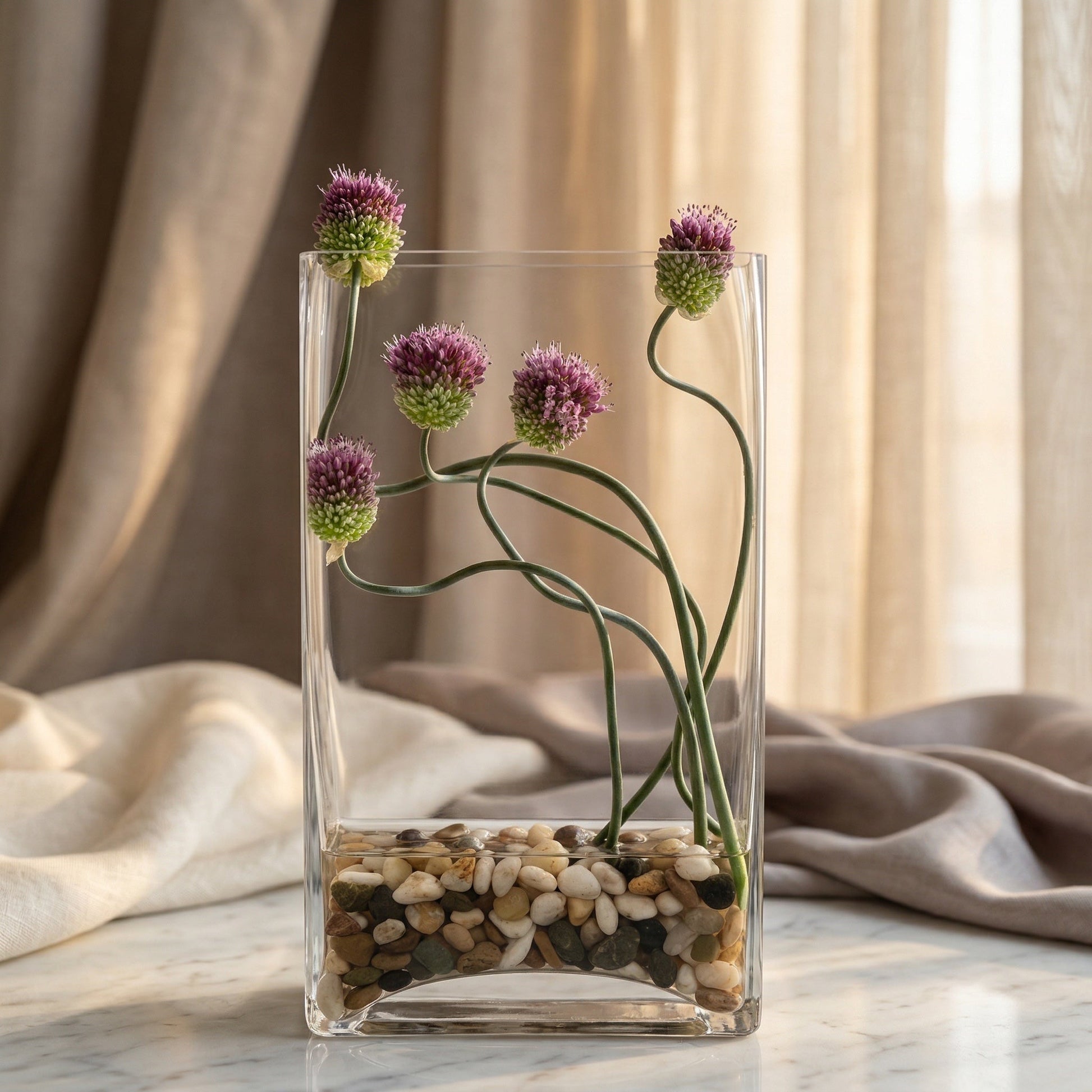 Purple allium flowers with curved stems in a clear glass vase with river stones - TJ Flowers NYC