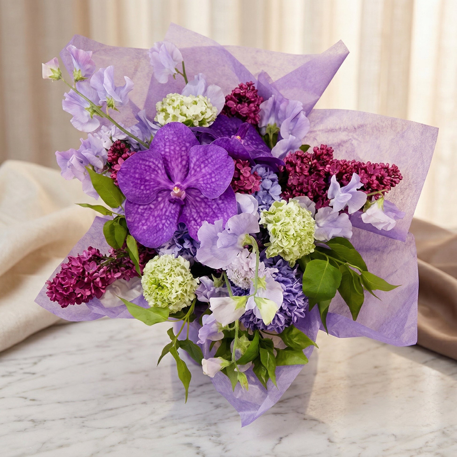 Purple Vanda orchid, lilac, and sweet pea bouquet wrapped in lavender paper on marble - TJ Flowers NYC