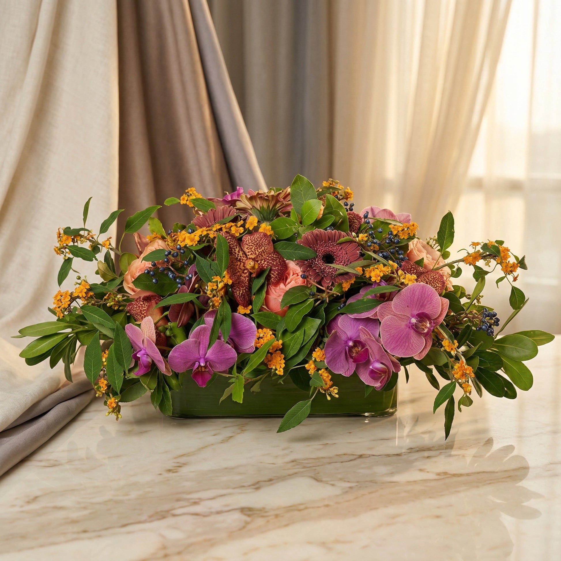 Purple orchids, pink roses, and orange filler flowers in a low glass vase on marble - TJ Flowers NYC
