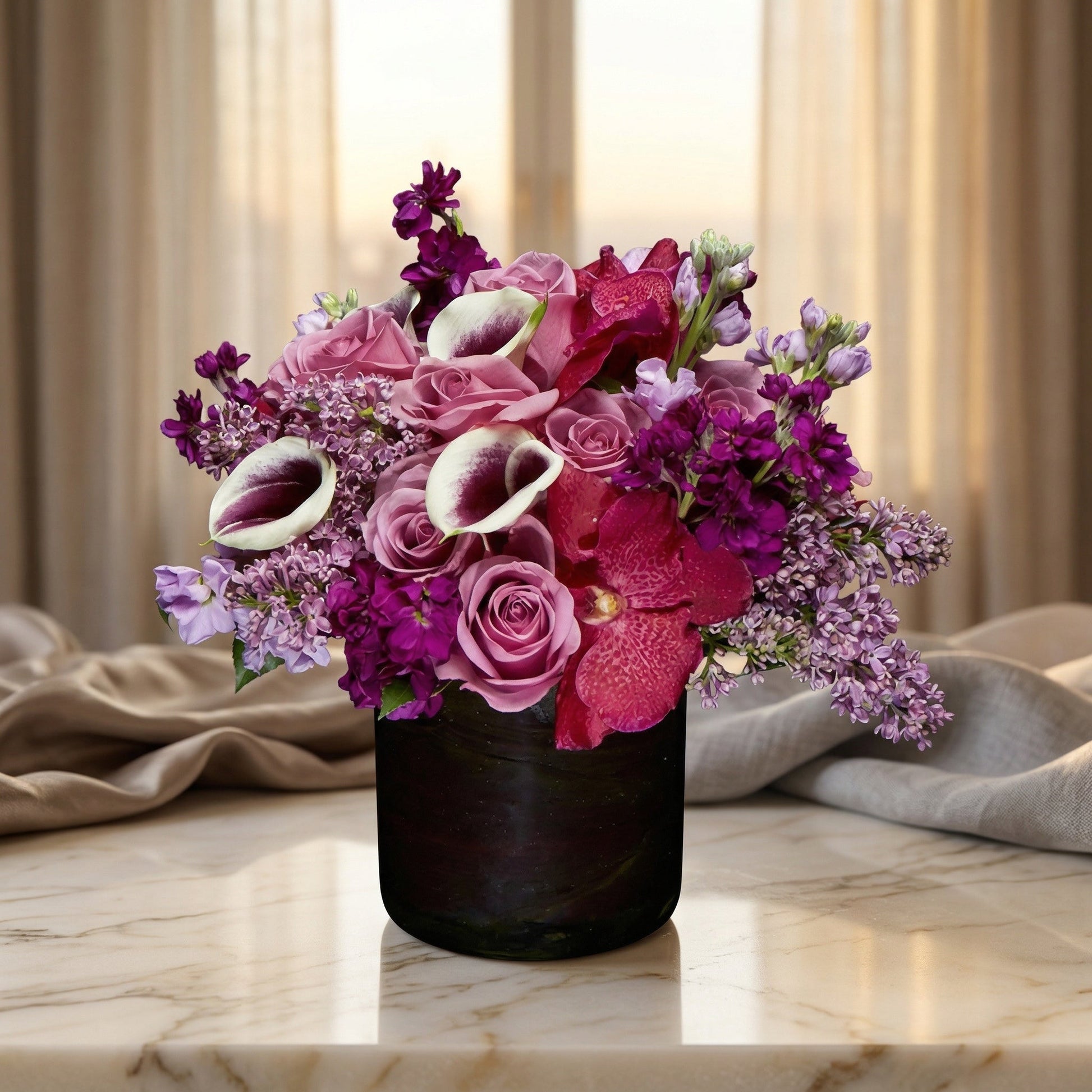 Purple and pink roses, orchids, and calla lilies in a dark vase on a marble table - TJ Flowers NYC