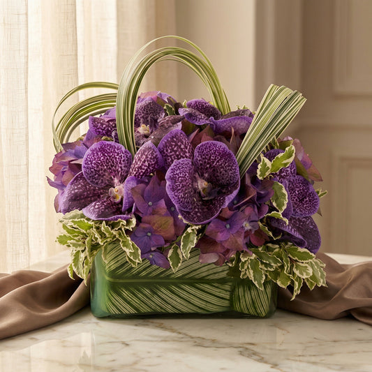 Purple vanda orchids and hydrangeas in a leaf-lined glass vase with variegated foliage - TJ Flowers NYC