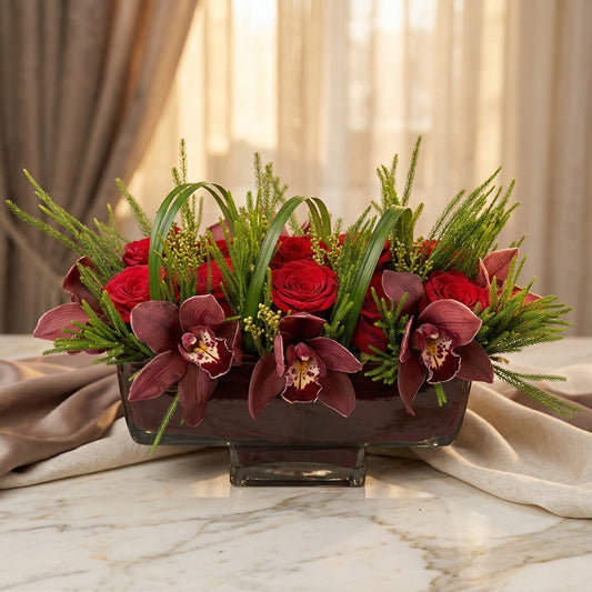 Red roses and burgundy cymbidium orchids in a dark rectangular glass vase with greenery - TJ Flowers NYC