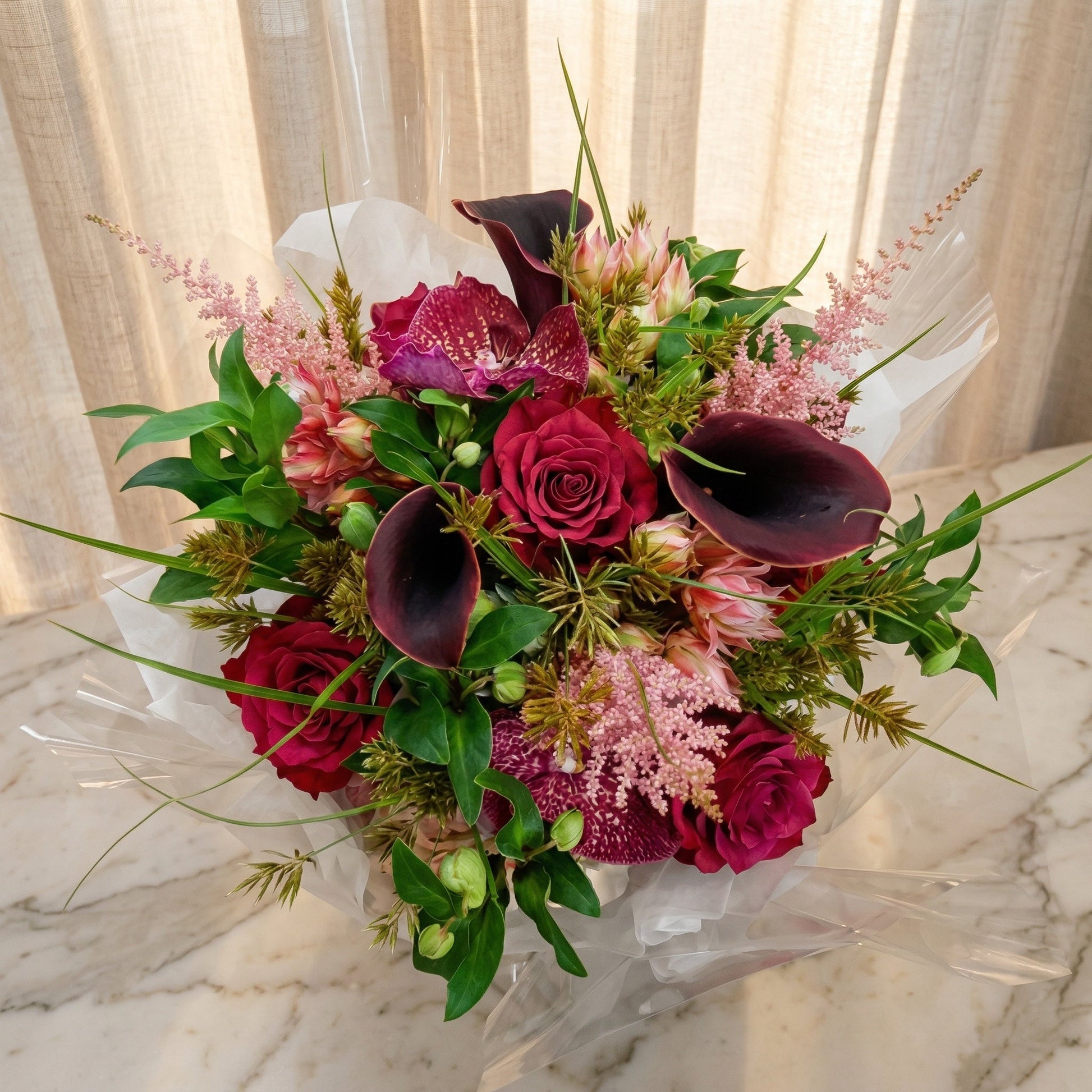 Deep red roses, purple orchids, and dark calla lilies in a wrapped bouquet - TJ Flowers NYC