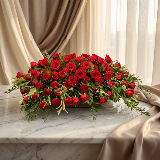 A large, low arrangement of vibrant red roses and greenery on a marble table. - TJ Flowers NYC