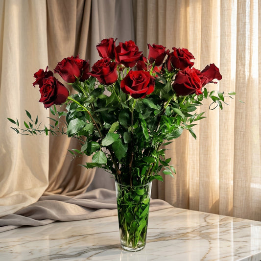 A dozen long-stemmed red roses in a clear glass vase on a marble table - TJ Flowers NYC