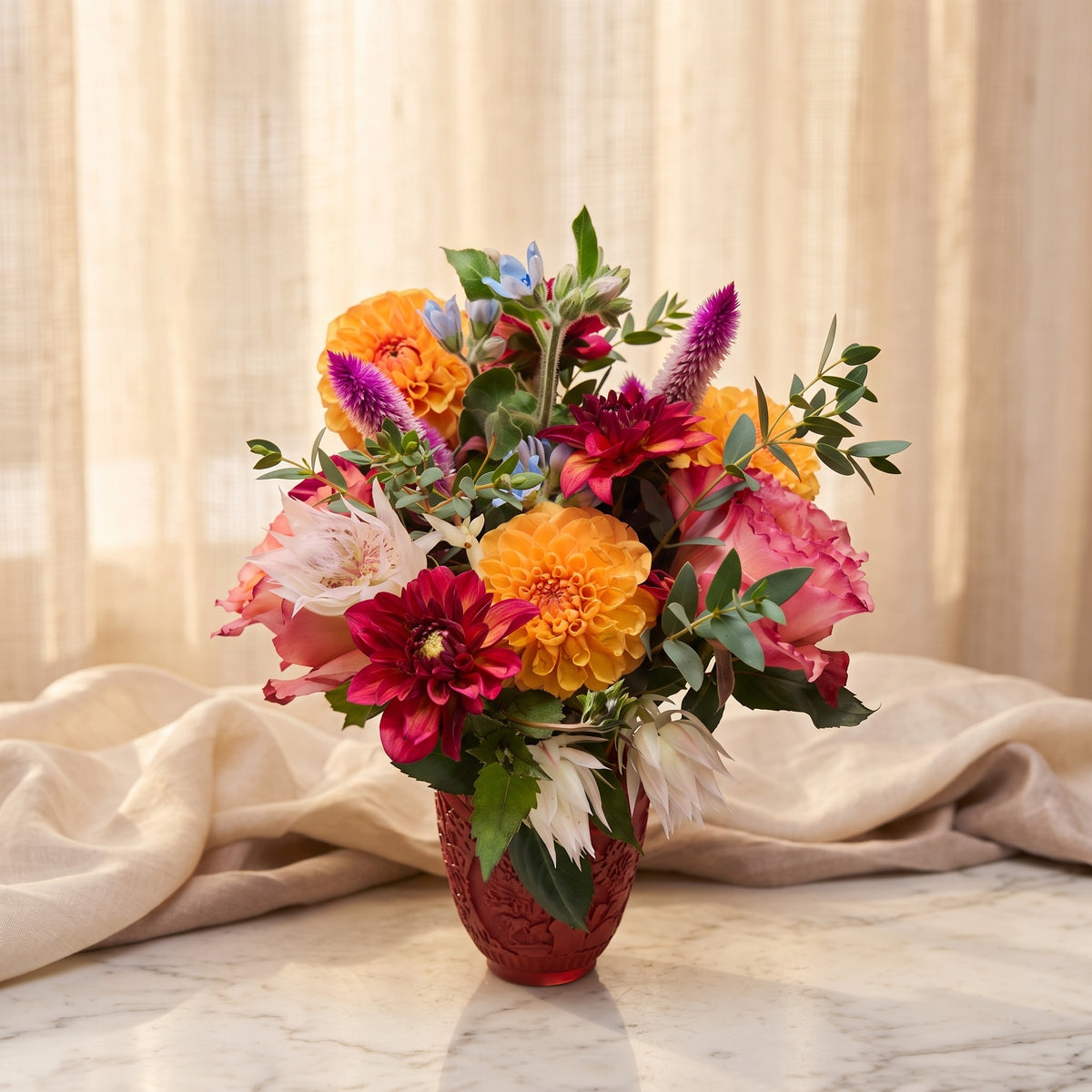 Orange and crimson dahlias with blushing bride protea and celosia in a ruby red glass vase - TJ Flowers NYC