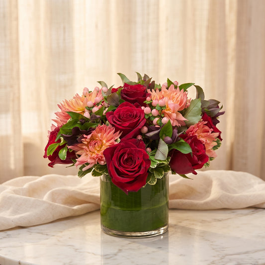 Red roses with peach cactus dahlias and blush hypericum berries in a leaf-lined glass vase - TJ Flowers NYC