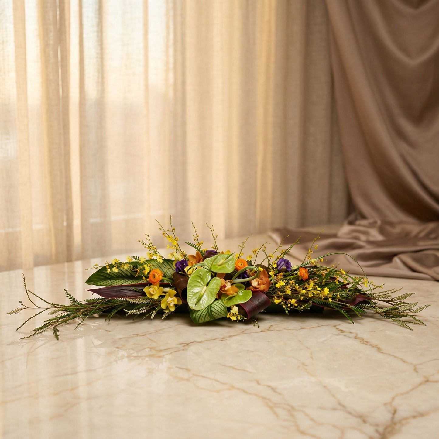 Low horizontal centerpiece with green anthurium, yellow orchids, and orange ranunculus on marble. - TJ Flowers NYC