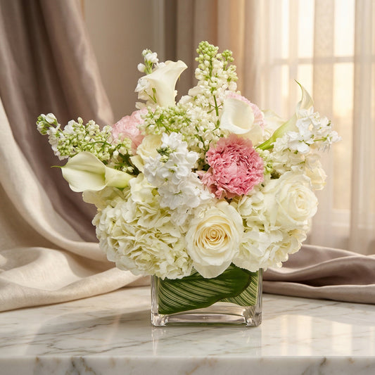 White roses, hydrangeas, and pink carnations in a square glass vase with a leaf wrap - TJ Flowers NYC