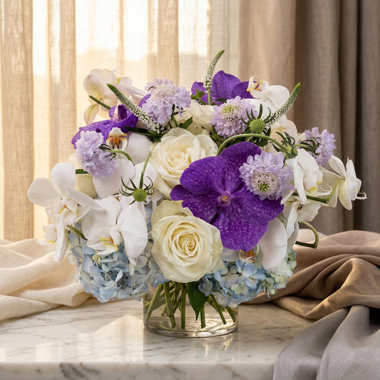 White roses, purple orchids, and blue hydrangeas in a clear glass vase - TJ Flowers NYC