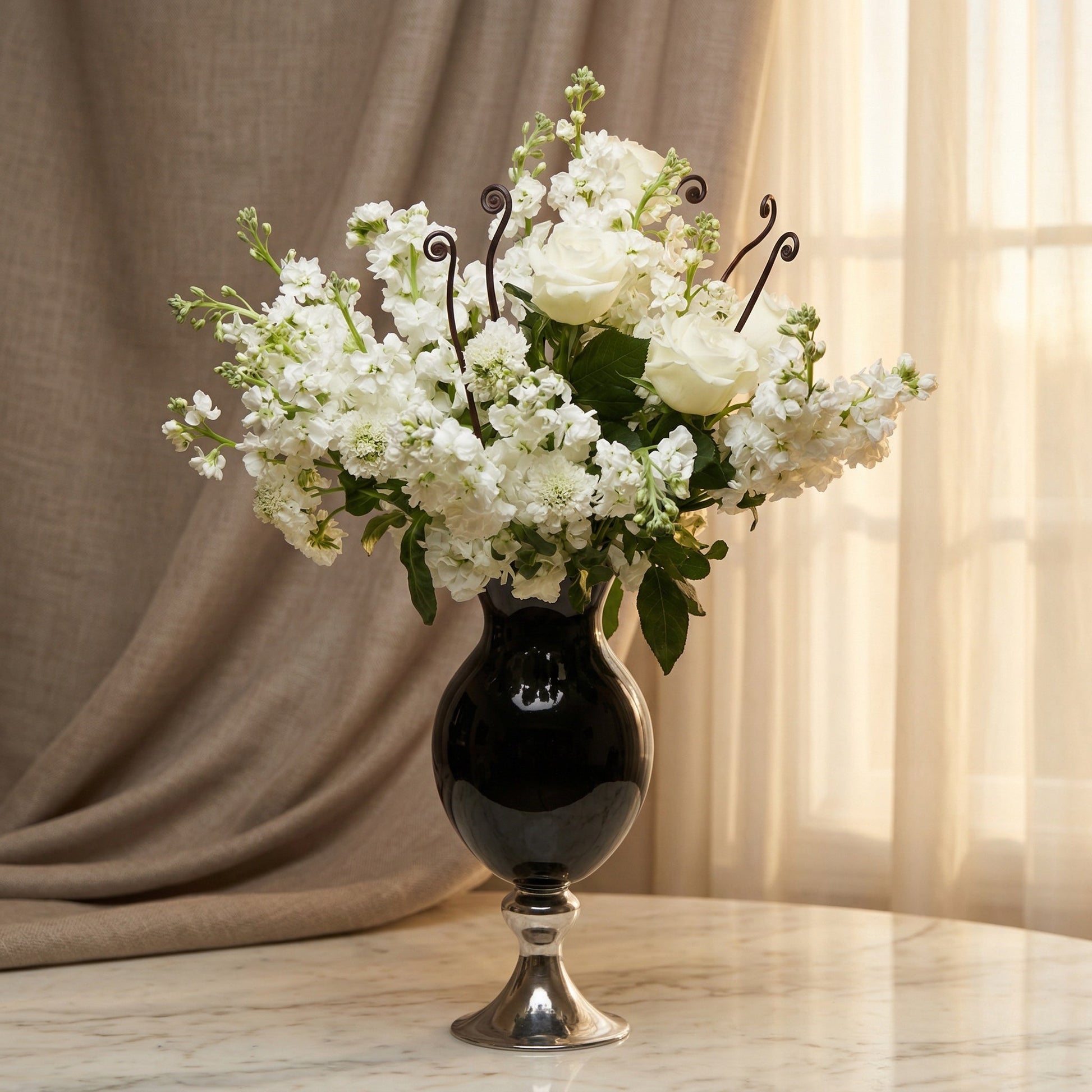Elegant white roses and stock flowers in a black and silver pedestal vase. - TJ Flowers NYC