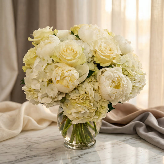 White roses, peonies, and hydrangeas in a clear glass vase on a marble table - TJ Flowers NYC