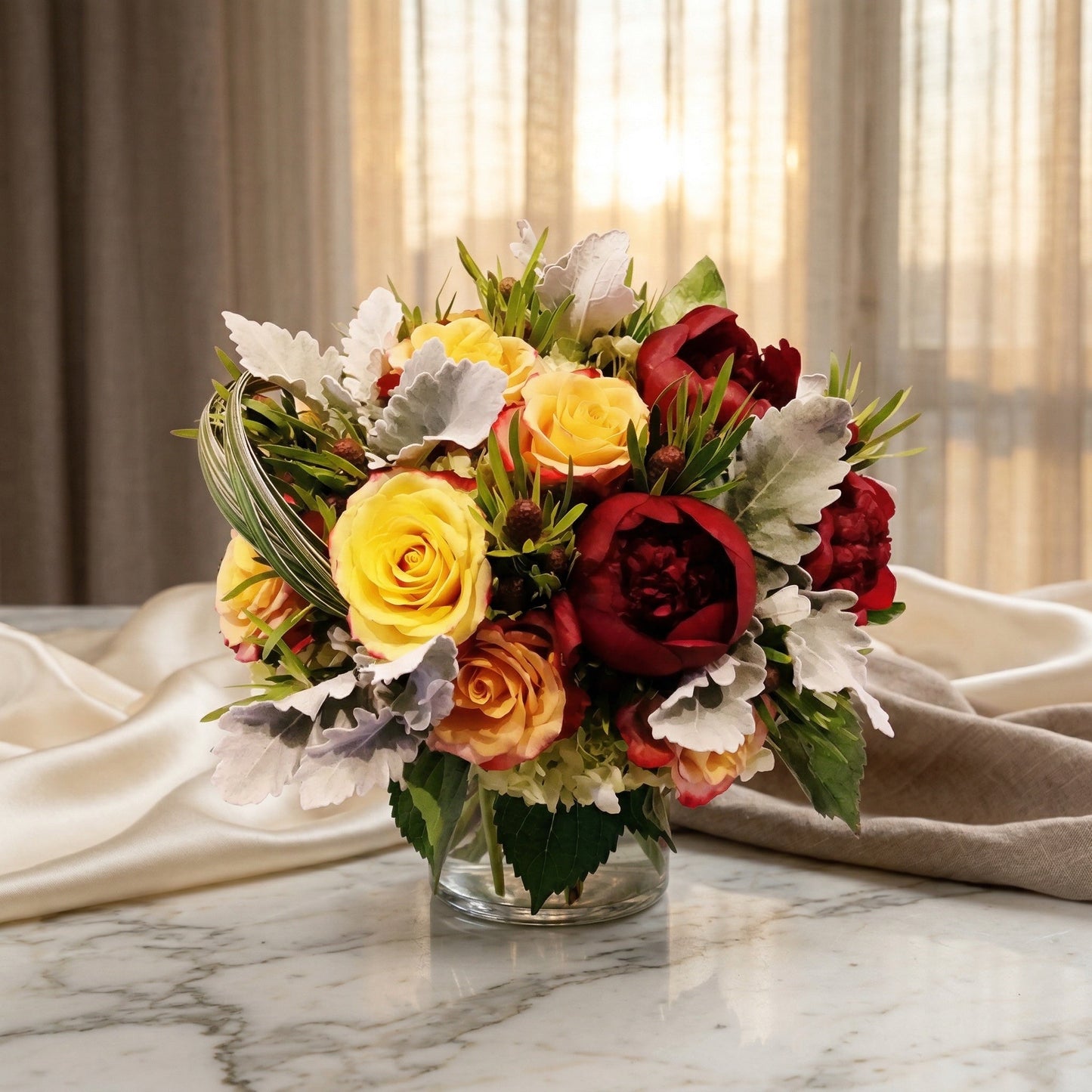 Yellow roses, deep red peonies, and dusty miller in a clear glass vase on a marble table - TJ Flowers NYC