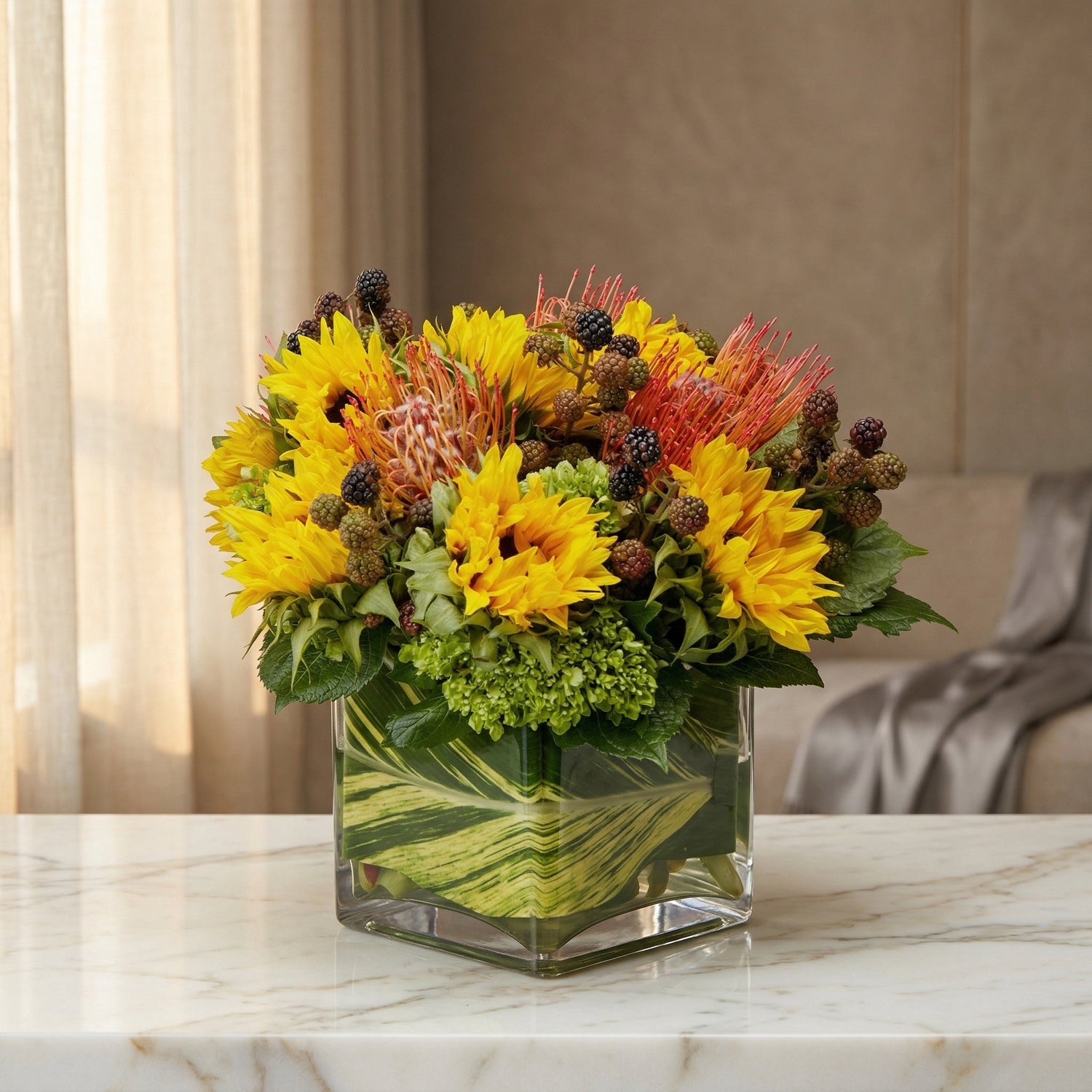 Yellow sunflowers, orange pincushion protea, green hydrangeas, and blackberries in a square glass vase - TJ Flowers NYC