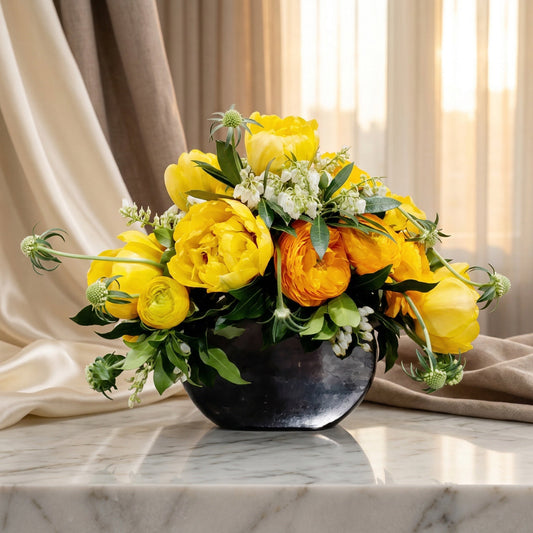 Yellow peonies, tulips, and ranunculus in a dark bowl vase on a marble table. - TJ Flowers NYC